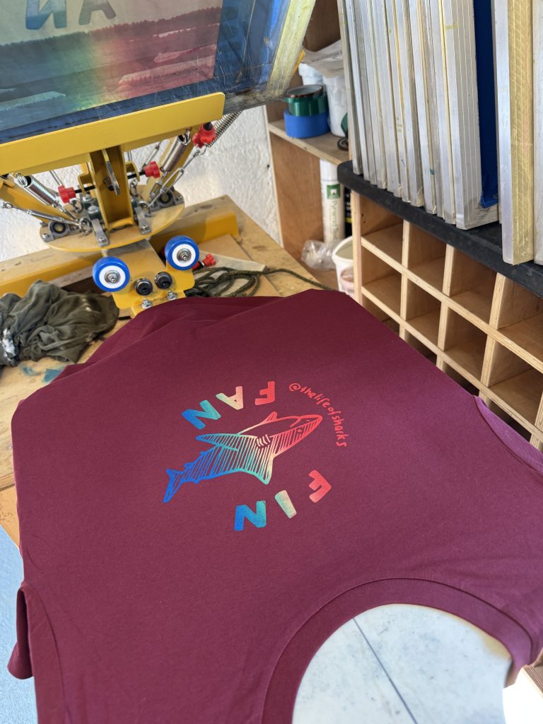 Close-up of a freshly screen printed rainbow Fin Fan design on a burgundy T-shirt