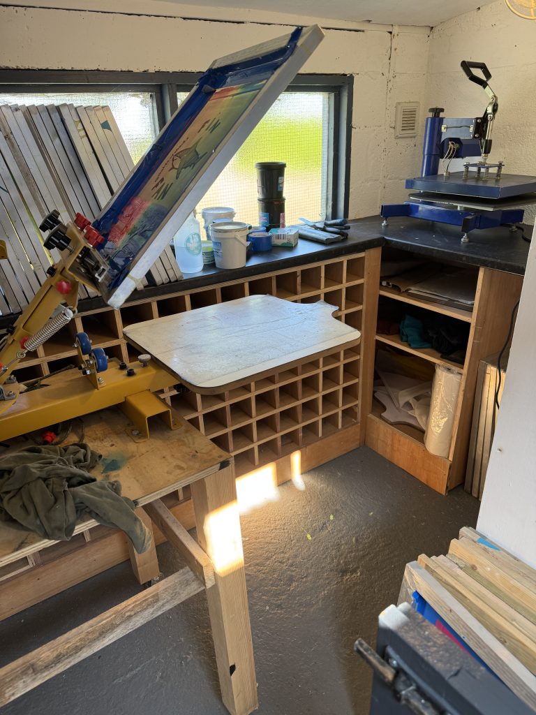 Inside The Life of Sharks print studio: screen printing press, racks of screens, inks and a heat press